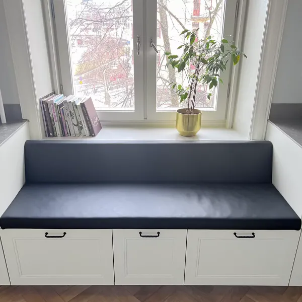 Sittdel med ryggstöd i svart vinylläder och lådfronter nedtill tillför både visuell elegans och praktisk funktion.